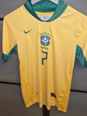 Brasilien matchtröja VINI JR #7 Nike - Gul Brasilien matchtröja från Nike med gröna detaljer, nummer 7 och VINI JR på ryggen. Tröjan har landslagets emblem på bröstet och klassisk sportig design med korta ärmar och rund hals. Perfekt för fotbollsfans som vill stötta sitt lag. Den är använd 1 gång. Pris är inget hugget i sten, kan snackas i DM. Priset är inte hugget i sten.