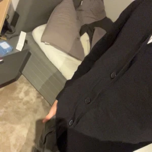 Svart kofta med knappar - En stilren svart kofta med knappar framtill. Koftan har lång ärm och en klassisk passform som funkar till många olika outfits. Perfekt för lager-på-lager och enkel att matcha med både jeans och kjol.