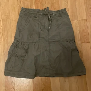 Kjol vintage y2k gullig från Kappahl <3 - Vintage lite y2k style kjol från Kappahl i storlek 36. Väldigt bra skick. Skulle dock säga att den passar S-M. Man kan reglera i midjan med hjälp av snöret. Snygga detaljer med knappar på fickorna och markerade sömmar. Passar perfekt till sneakers eller boots, speciellt nu till hösten!