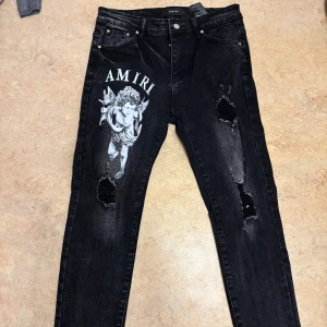 Svarta Amiri jeans med ängeltryck - Svarta jeans från Amiri med vit ängelgrafik och logga på vänster lår. Snygga slitningar och hål på båda benen ger en edgy look. Klassisk femficksmodell med smal passform och detaljer i silver. Perfekta för dig som vill sticka ut.