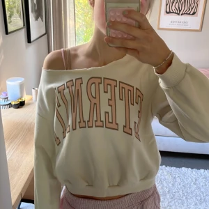 Offshoulder vit sweatshirt ETERNITY - Vit croppad sweatshirt med offshoulder-passform och trycket 'ETERNITY' i beige och brunt framtill. Tröjan har bred resår i midjan och rå kant upptill för en avslappnad vibe. Perfekt för dig som gillar en loose och trendig stil. Är från hm men klippt själv därav finns ingen lapp😊 Andvänd helst inte köp direkt utan skriv först tack