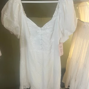 Vit kortklänning med puffärm från Nelly - En vit klänning från Nelly med puffiga armar i storlek 44. Den har knappar framtill och en dragkedja där bak. Aldrig använts då den är lite för stor💗