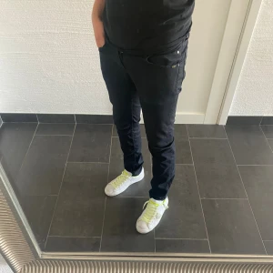 Svarta jeans från Tiger of Sweden - Säljer ett par svarta jeans från Tiger of Sweden. Modellen är slim fit med klassisk femficksdesign och diskret logga bak i midjan. Jeansen har en snygg, smal passform och är tillverkade i ett mjukt bomullstyg med stretch för extra komfort.