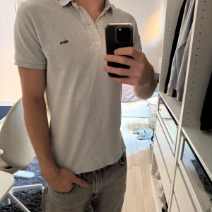Grå pikétröja från Lacoste - Säljer en klassisk grå pikétröja från Lacoste, väldigt bra skick! Storlek M, passar även S👏🏼