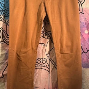 Bruna chinos från AVVA Jeans, stl 42 - Snygga bruna chinos från AVVA Jeans i storlek 42. Byxorna är tillverkade i bomull och har klassisk rak passform med diskreta bakfickor och bälteshällor. Perfekta för en clean och stilren look.