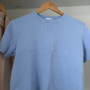 Ljusblå ribbad t-shirt från H&M - Snygg ljusblå t-shirt från H&M med ribbad struktur och rund hals. Modellen är kortärmad och har en clean, enkel look som är lätt att matcha. Den är perfekt för dig som gillar kortare t-shirts och som gillar stilrena och fräscha färger.