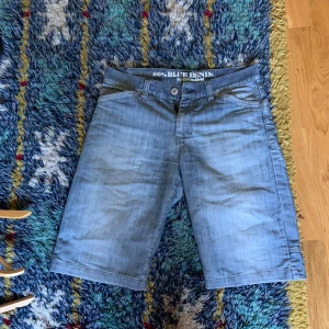 Blå jeansshorts från Cottonfield - Säljer ett par klassiska blå jeansshorts från Cottonfield. De har fem fickor, bälteshällor och stängs med knapp och dragkedja. Perfekta för sommaren med sin avslappnade passform och ljusa denimtvätt.