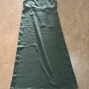 Grön långklänning med knyt från H&M - Snygg grön långklänning från H&M med tunna axelband och knyt i midjan. Klänningen har en lätt glansig yta och är tillverkad i ett mjukt, tunt material som ger en elegant känsla. Perfekt för dig som gillar stilrena och enkla plagg med en twist.