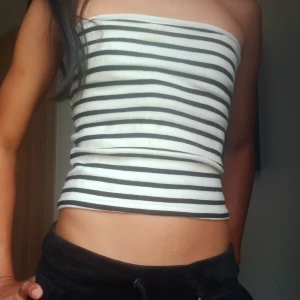 Randig bandeau tubtopp i bomull - Säljer en snygg bandeau tubtopp med svarta och vita horisontella ränder. Toppen är ärmlös och croppad, perfekt för varma dagar. Tillverkad i mjuk och stretchig bomull som sitter skönt mot kroppen. Enkel och stilren design som är lätt att matcha.