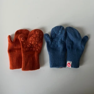 Blå och orange tumvantar från PAX - Två par tumvantar från PAX, ett par i blått och ett par i orange. Båda har stjärnmönster på handflatan för extra grepp. Vantarna är stickade och tillverkade av ull, polyester och syntetmaterial. 