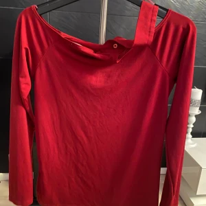 Röd oneshoulder långärmad topp BikBok - Snygg röd långärmad topp från BikBok i oneshoulder-modell med en axelrem och bred halsringning. Tillverkad i mjuk bomull som känns skön mot huden. Perfekt för dig som vill sticka ut med en cool och trendig look.