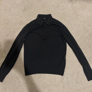 Mörkgrå stickad långärmad pikétröja Uniqlo - Mörkgrå stickad pikétröja från Uniqlo med klassisk krage och tre knappar framtill. Tröjan är långärmad och har en stilren, enkel design som funkar till många olika looks. Materialet känns mjukt och lätt, perfekt för dig som gillar minimalistisk stil.