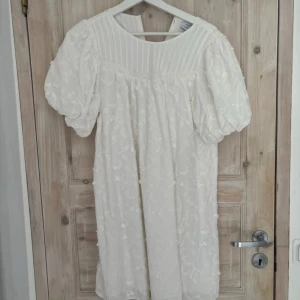 Studentklänning - Superfin vit klänning från & Other Stories med broderade blommor, puffärmar och knappar i ryggen. Klänningen har en kort längd, rund hals och romantiska spetsdetaljer upptill. 