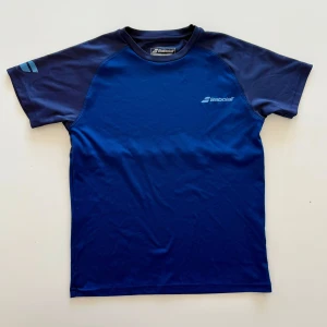 Svarta sportshorts från Babolat - Säljer ett par svarta sportshorts från Babolat med elastisk midja och diskret logga på ena benet. Shortsen är gjorda i ett lätt och snabbtorkande syntetmaterial, perfekta för intensiva träningspass eller tennis. sen också 2 tränings tshirtar.