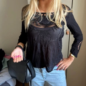 Svart blus med spetsdetaljer från hunkydory  - Svart blus med transparenta partier och broderade spetsdetaljer. Långärmad modell med dekorativa hål längs ärmar och halsringning. Luftigt tyg och avslappnad passform, perfekt för dig som gillar en stilren men ändå unik look. Strl xs men passar s. Knappt använd 