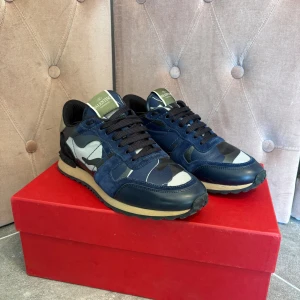 Valentino Garavani Rockrunner sneakers - Snygga Valentino Garavani Rockrunner sneakers i marinblått och grått med camouflage-mönster. Skorna har svarta snören, detaljer i mocka och skinn samt en beige sula med nitar vid hälen. Perfekt för dig som vill sticka ut med exklusiva och trendiga sneakers. Skick : 8/10✅ kommer med box, dustbag & äkthetsintyg✅