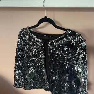 Svart paljettopp från Bik Bok - Glittrig svart topp från Bik Bok, täckt med silvriga paljetter som reflekterar ljuset. Modellen är croppad med trekvartsärm och rund halsringning. Perfekt för dig som vill sticka ut och glänsa på festen. 💘💘🥃🥃
