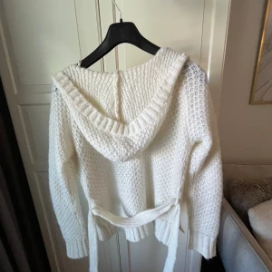 Vit stickad kofta med luva - Mysig vit stickad kofta från ONLY med luva och knytskärp i midjan. Koftan har grovstickat mönster och långa ärmar använd 2 gånger 