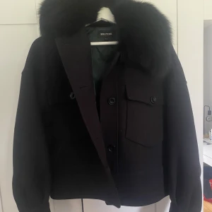 Svart meotine jacka - Svart kort kappa från Meotine med päls. Jackan har lite noppror men inget tydligt, två stycken små lösa trådar. Men annars har jackan inga tydliga defekter 