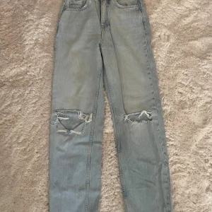 Ljusblå ripped jeans med raka ben -  Ljusblå jeans från Gina Tricot med raka ben, hög midja och slitna detaljer över knäna. Storlek 34
