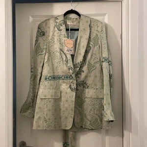 Mönstrad kavaj med bälte Odd Molly - Superfin ljusgrön kavaj från Odd Molly med unikt mönster i grönt och blått. Kavajen har knappar framtill, två fickor och ett matchande bälte i midjan. Snygg passform och coola detaljer som ger en personlig touch. Perfekt för dig som vill sticka ut med stil.