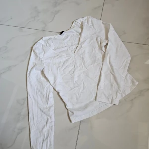 Vit långärmad topp med v-ringning xs/s - En enkel och stilren vit långärmad topp med v-ringad hals. Tillverkad i mjuk bomull som känns skön mot huden. Perfekt att matcha med jeans eller kjol för en clean look.