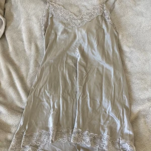 Ljusgrå satin nattlinne Intimissimi - Supersöt ljusgrå slipklänning från Intimissimi i satin med spetsdetaljer vid urringning och nederkant. Klänningen har smala justerbara axelband och en mjuk, glansig finish som känns lyxig. Perfekt för dig som gillar en enkel men elegant look. Har digert kolla sista bilden