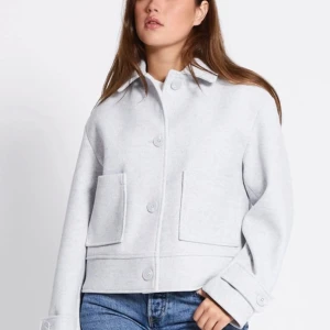 Grå kort kappa från 157, storlek M - Snygg grå kort kappa från 157 lager i boxig modell med stora fickor framtill och klassisk krage. Jackan har knäppning med stora knappar och breda ärmslut med knappdetalj. Perfekt att slänga över en hoodie eller t-shirt för en chill look.