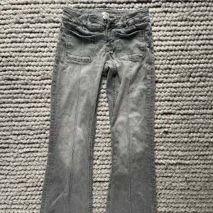 Grå snygga low waiat utsvängda jeansbyxor från Gina Tricot  - Grå snygga o coola jeansbyxor från Gina Tricot i storlek 152. Byxornar utsvängda med stora framfickor och klassiska bakfickor. De är tillverkade i ett mjukt bomullsmaterial med en cool tvättad look och har bälteshällor och dragkedja framtill.