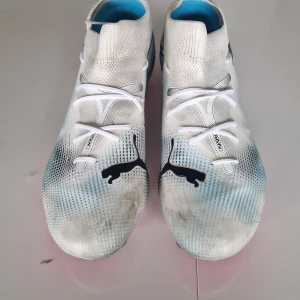 Puma vita och rosa fotbollsskor storlek 40.5 - Snygga fotbollsskor från Puma i vitt med svarta detaljer och coolt blått mönster. Skorna har rosa dobbar och sula, samt stora FR-tryck på sidan. Ovandelen är i syntetmaterial och har snörning för bra passform. Perfekta för dig som vill sticka ut på planen. Andvänds 3 gånger.