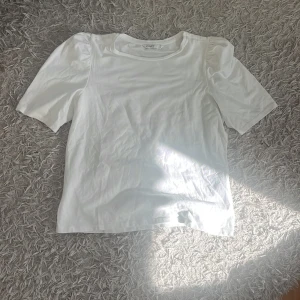 Vit puffärm topp från ONLY - Säljer en stilren vit topp från ONLY med puffärmar och rund halsringning. Toppen har en rak passform och är gjord i mjuk bomull, perfekt för en clean och enkel look. Passar dig som gillar minimalistisk stil och vill ha något som funkar till allt.