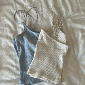 Ribbad linne-topp med tunna axelband - Två ribbade linne-toppar med tunna dubbla axelband, en i ljusblått och en i vit. Snygg croppad passform och stretchigt ribbat material. Köpa från lager 157 med bortklippta lappar. Storlek: XXS/XS