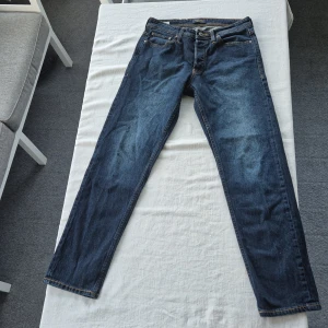 Blå jeans Jack & Jones  - Snygga blå jeans från Jack & Jones, modell Comfort/Mike. Klassisk femficksdesign med kontrastsömmar och raka ben. Jeansen har en normal passform och är tillverkade i slitstarkt denimtyg. Perfekta för en avslappnad och stilren look.