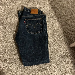 Levi's 501 mörkblå jeans W27 L30 - Klassiska Levi's 501 jeans i mörkblå tvätt med raka ben och femficksmodell. Snygga kontrastsömmar och ikonisk läderpatch bak i midjan. Jeansen är tillverkade i robust denim och har knappgylf. Perfekta för en avslappnad och tidlös stil. priset kan diskuteras vid en snabb affär