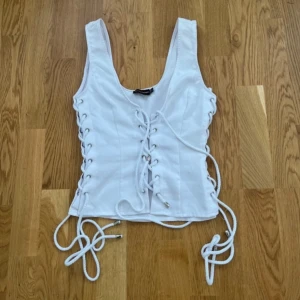 Vit korsettopp med snörning - Snygg vit korsettopp med breda axelband och snörning framtill och på sidorna. 