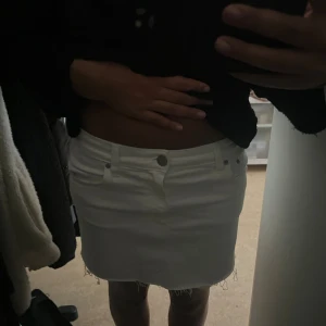 Vit jeanskjol med fransig kant - Säljer en vit kort jeanskjol med rå fransig kant nertill och klassiska fickor fram och bak. Kjolen har bälteshällor och stängs med knapp och dragkedja. Perfekt för dig som gillar en clean och enkel stil med edge.