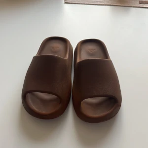 Adidas Yeezy Slide Flax strl 37 - Säljer ett par Adidas Yeezy Slide i färgen Flax. Slidesen är bruna med chunky, ribbad sula och öppen tå. Tillverkade i syntetmaterial för en mjuk och bekväm känsla. Perfekta för chill dagar eller när du vill ha en clean och trendig look.                            Skorna står i storlek 38 men är små i storleken och känns mer som 37-36,5