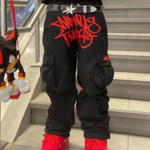 Svart röda minus two cargopants - Svarta cargopants med avtagbara ben, så de kan bäras som shorts. Stora fickor på sidorna och fet röd graffiti-text framtill. Rå streetkänsla och loose fit, perfekt för dig som vill sticka ut. Materialet är bomull och detaljerna är riktigt snygga. Och texten är sydd