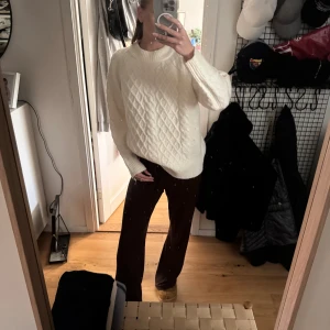 Vit stickad tröja med kabelmönster - Säljer en vit stickad tröja med snyggt kabelmönster och rund hals. Tröjan har en loose passform och långa ärmar, perfekt för att hålla sig varm och ändå se chill ut. Passar dig som gillar klassisk stil med en modern twist.