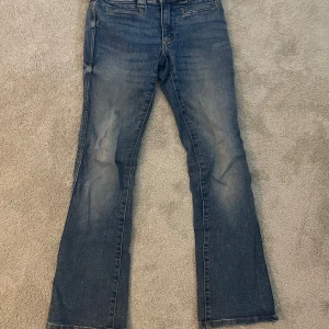 Blå bootcut jeans från H&M, stl 140 - Snygga blå bootcut jeans från H&M med låg midja och justerbar midja. Jeansen har klassisk femficksdesign med coola ficklock bak och slitningar för en avslappnad look. Perfekta för dig som gillar retrovibbar och bekväm passform.