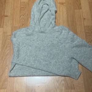 Ljusgrå merinoull hoodie - Mysig ljusgrå hoodie i stickat material med huva och långa ärmar. Perfekt för att chilla hemma eller dra över en t-shirt när det är kyligt. Enkel och stilren design utan tryck eller detaljer.
