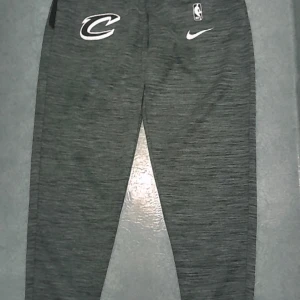 Grå Nike NBA Dri-Fit mjukisbyxor M - Snygga grå mjukisbyxor från Nike med Cleveland Cavaliers-logga och NBA-märke. Byxorna är i Dri-Fit-material som andas och har en sportig look med smal passform. Perfekta för dig som gillar basket eller vill ha en chill streetstyle.