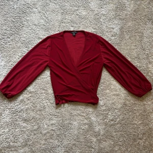 Vinröd omlottopp från Amisu - Snygg vinröd omlottopp från Amisu med långa ärmar och djup v-ringning. Toppens omlottdesign ger en schysst siluett och den är tillverkad i ett mjukt, stretchigt material som sitter bekvämt. .