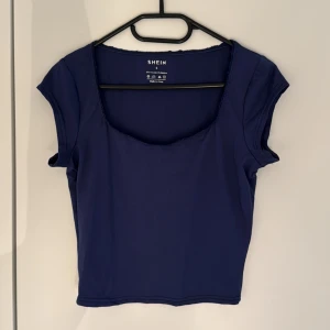 Mörkblå croppad topp från SHEIN - Säljer en mörkblå croppad topp från SHEIN i stretchigt material. Toppen har korta ärmar, fyrkantig ringning med rå kant och är tillverkad i 95% polyester och 5% elastan. Perfekt för dig som gillar enkel men snygg stil. Aldrig använd 