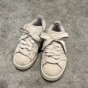 Adidas 00s ljusrosa - Snygga ljusrosa adidad skor med klassiska tre ränder på sidan och breda snören. Låg modell med rund tå och vit sula. Perfekta för dig som gillar en clean och stilren look