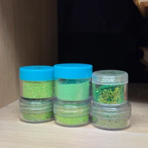 Gröna glitter i burkar  - Säljer 6 burkar med grönt lösglitter i olika nyanser och storlekar på glitterkornen. Kommer i små runda plastburkar med blå eller transparent lock.Kommer i små genomskinliga plastburkar. Burkarna kan ha repor pga att ha legat bland andra produkter och märkta med något nummer, men det är inga problem med produkterna. 