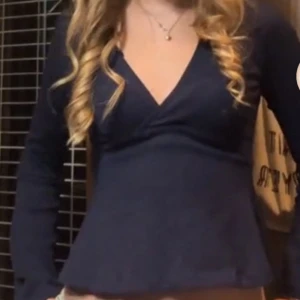 Marinblå v-ringad topp med knytband - Säljer en marinblå v-ringad topp med långa vida armar. Toppen har dn fin v-ringing och baksidan knyts med ett ganska brett band. Bra kvalité på toppen, inte använd särskilt många gånger. Den känns lite större i storleken än vad den är. 