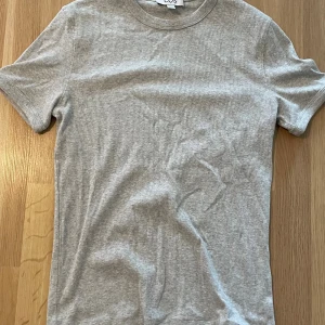 Två ribbade t-shirts från COS - Säljer två stilrena t-shirts från COS i storlek S. En är ljusgrå och den andra är marinblå, båda i mjuk bomull med klassisk rund hals och korta ärmar. Perfekta att matcha med jeans eller shorts för en clean look. Ny pris 400, 200 st eller 300 för båda