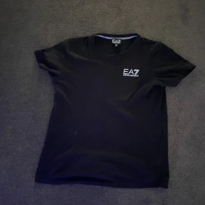 Svart EA7 t-shirt med logga - Svart t-shirt från EA7 Emporio Armani med vit logga tryckt på bröstet. korta ärmar. Mjuk och skön bomull.