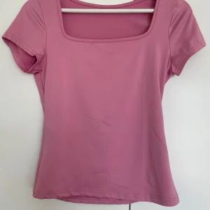 Rosa topp med fyrkantig ringning - En stilren rosa topp med korta ärmar och fyrkantig ringning. Toppen är figurnära och tillverkad i ett mjukt, stretchigt material som känns skönt mot huden. Perfekt för dig som gillar en enkel men snygg look.